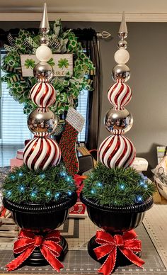 two christmas decorations on top of black pots with red and white striped balls in them