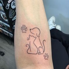 a dog and cat tattoo on the left arm with paw prints in black ink, sitting next to a person's leg