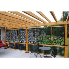 an outdoor patio with chairs and table next to a pergolated wall that has trees on it