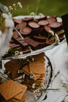 chocolate and crackers are arranged on a glass platter with flowers in the background