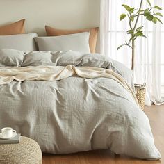 a bed with pillows and blankets on top of it next to a potted plant