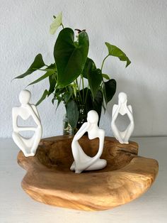 three white figurines are sitting in front of a potted plant on a wooden tray