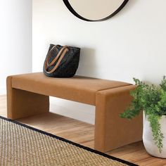 a brown bench sitting next to a plant in a white vase on top of a hard wood floor