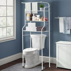 a white toilet sitting next to a bathroom shelf filled with towels and other items on top of it