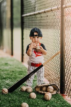 a little boy that is standing in the grass with a baseball bat and some balls