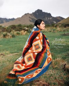 a woman is sitting on the grass wearing a blanket