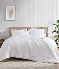 a bed with white sheets and pillows in a room next to a potted plant