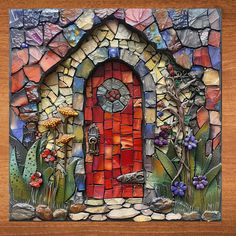 a mosaic art piece with a red door surrounded by plants and flowers on a wooden surface