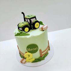 a green cake decorated with a tractor and farm animals on the top is sitting on a white table