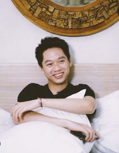 a man sitting on top of a bed next to a mirror and pillows in front of him