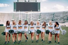 a group of cheerleaders standing on top of a field in front of a stadium