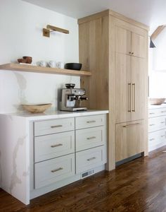 a kitchen with white cabinets and wood flooring on the walls, along with wooden shelves