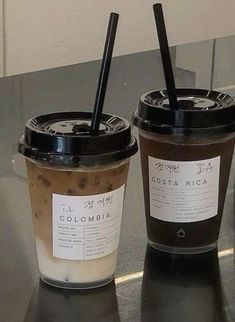 two coffee cups sitting next to each other on top of a metal counter with black straws