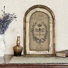 there is a vase with flowers on the table next to an old fashioned frame and some books