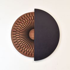 a wooden clock with black and brown designs on the face, sitting against a white wall