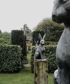 a statue of a rabbit sitting on top of a wooden post in front of hedges