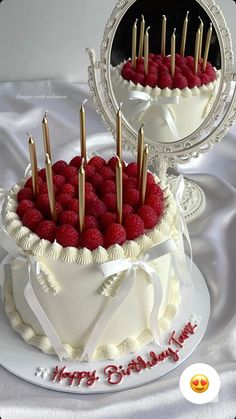 a white cake topped with raspberries on top of a table next to a mirror