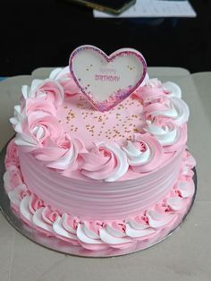 a pink and white birthday cake with a heart on top