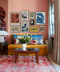 a living room with pink walls and pictures on the wall above the couch, along with a coffee table