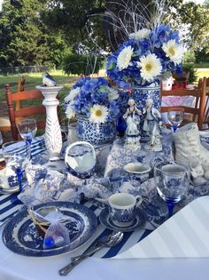 a blue and white table setting with flowers in vases on the centerpiece, plates and utensils