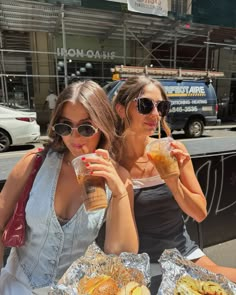 two women sitting at a table with sandwiches and drinks