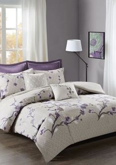 a bed with purple and white comforters in a room next to a lamp on a table