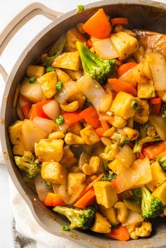 a pan filled with stir fry vegetables on top of a white cloth next to a wooden spoon