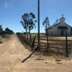 an old church sits on the side of a dirt road in front of a fence