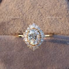 an engagement ring sitting on top of a cushioned surface with the diamond center surrounded by smaller round diamonds