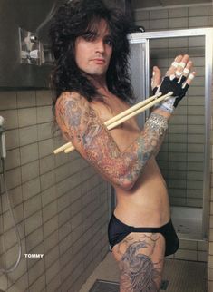 a man with long hair and tattoos holding two sticks in his hand while standing next to a shower