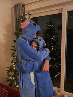 two people in blue costumes hugging each other near a christmas tree with lights on it