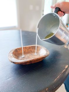 a person pouring water into a wooden bowl on top of a table with two sticks sticking out of it