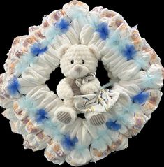 a white teddy bear sitting on top of a blue and white diaper wreath with ruffles