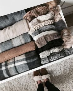 a person standing in front of a drawer filled with folded blankets and sweaters on the floor