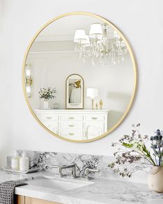 a white bathroom with marble counter tops and a round mirror on the wall above it