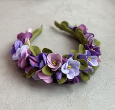 a close up of a flower headband on a white surface with purple and green flowers