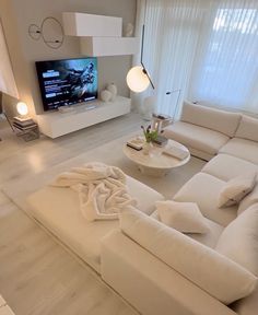 a living room filled with white furniture and a flat screen tv mounted on the wall