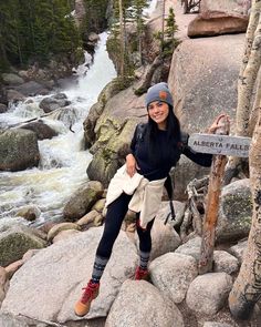 a woman sitting on top of a rock next to a river and holding onto a sign