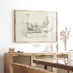 a drawing hangs above a dining table with wicker chairs