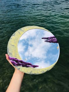 a hand holding up a circular mirror over water