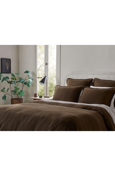 a bed with brown sheets and pillows in a bedroom next to a plant on the wall