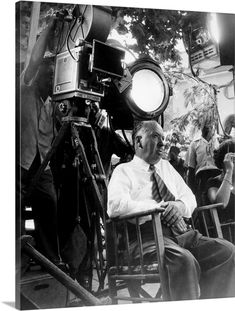 a man sitting in a chair next to a camera and another man standing behind him