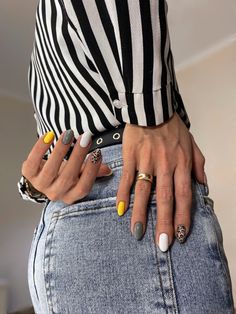 a woman's hands with yellow and white nail polishes on her fingers, standing in front of a black and white striped shirt