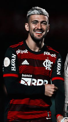 a soccer player is smiling and wearing a black and red uniform with white lettering on it