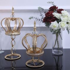 two gold crowns sitting on top of a black table next to white flowers and vases