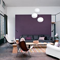 a living room filled with furniture next to a purple wall and two white lamps hanging from the ceiling