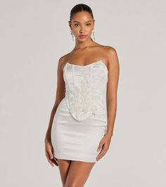 Chic with a stunning allure, the Hannah pearl beaded floral satin corset mini dress is an iconic choice for homecoming or your next formal party. Crafted with sleek satin woven fabric with a knit lining, she showcases a gorgeous embroidered floral applique accented with mini faux pearls, sequins, and beaded embellishments in an intricately placed design. The short dress features a strapless square neckline, a fitted corset bodice overlay with flexible boning to provide structure, a bold open lac Hoco Dress Windsor, White Satin Corset Dress For Cocktail, Fitted Corset For Homecoming, Satin Corset Dress With Fitted Bodice For Homecoming, Satin Corset Dress For Party Season, Satin Corset Dress For Homecoming And Prom Season, Satin Corset Dress For Homecoming And Prom, Corset Mini Wedding Dress, Satin Mini Dress With Corset Back For Wedding