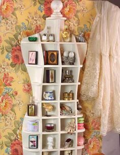 a white shelf filled with lots of items next to a floral wallpapered wall