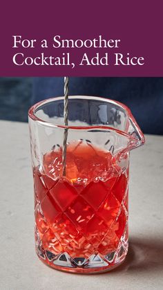 a glass pitcher filled with red liquid sitting on top of a table next to a straw