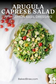 a salad with lemon basil dressing on a white plate next to some tomatoes and other vegetables